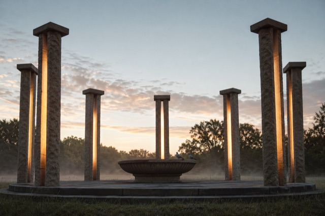 The pillar circle photographed at first light, mist hanging at ankle height, a pair of doves on the rim of the fountain.